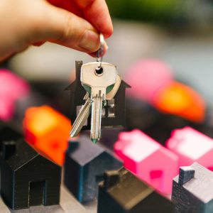 Colorful miniature houses and a hand holding keys representing real estate decisions.