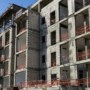 A modern multi-story apartment building under construction with scaffolding and safety netting.
